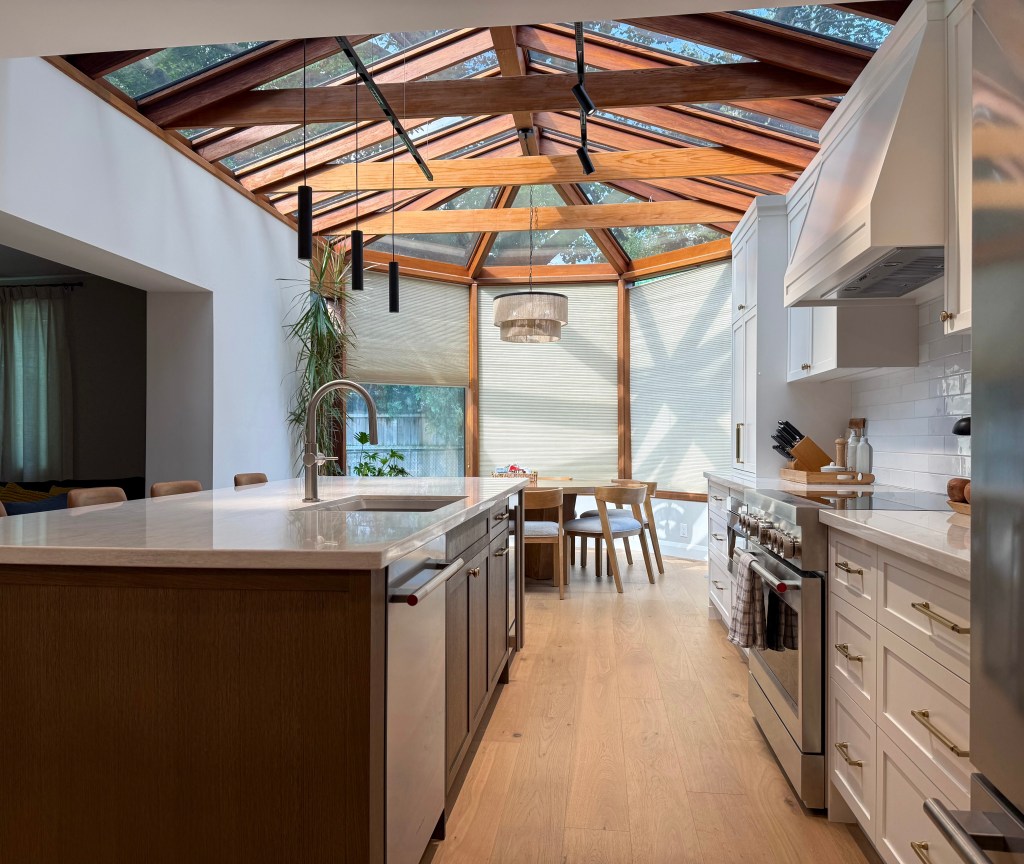 Renovated Toronto kitchen with white cabinetry, wood island and suspended lighting beneath a glass-and-timber ceiling. 